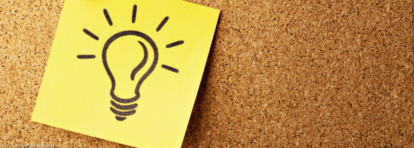 Ein gelber Zettel mit einer gezeichneten leuchtenden Glühbirne auf einer Korktafel