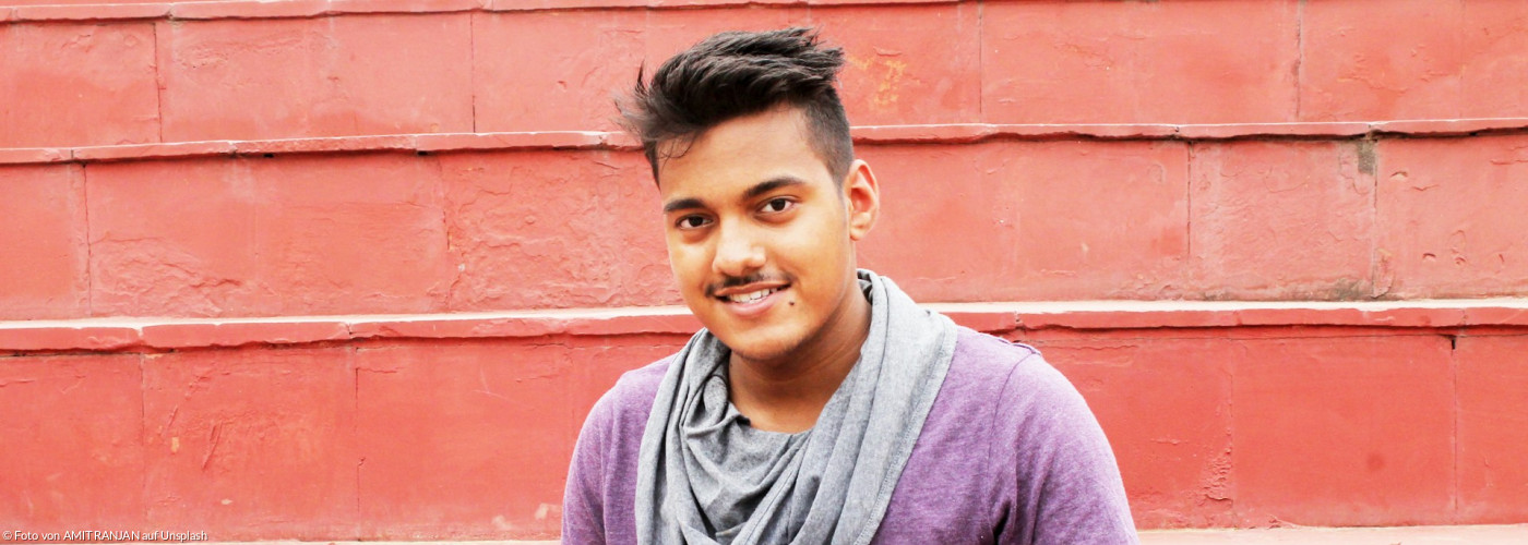 Pereson in lila Hemd und blauer Jeans sitzt auf Betonbank