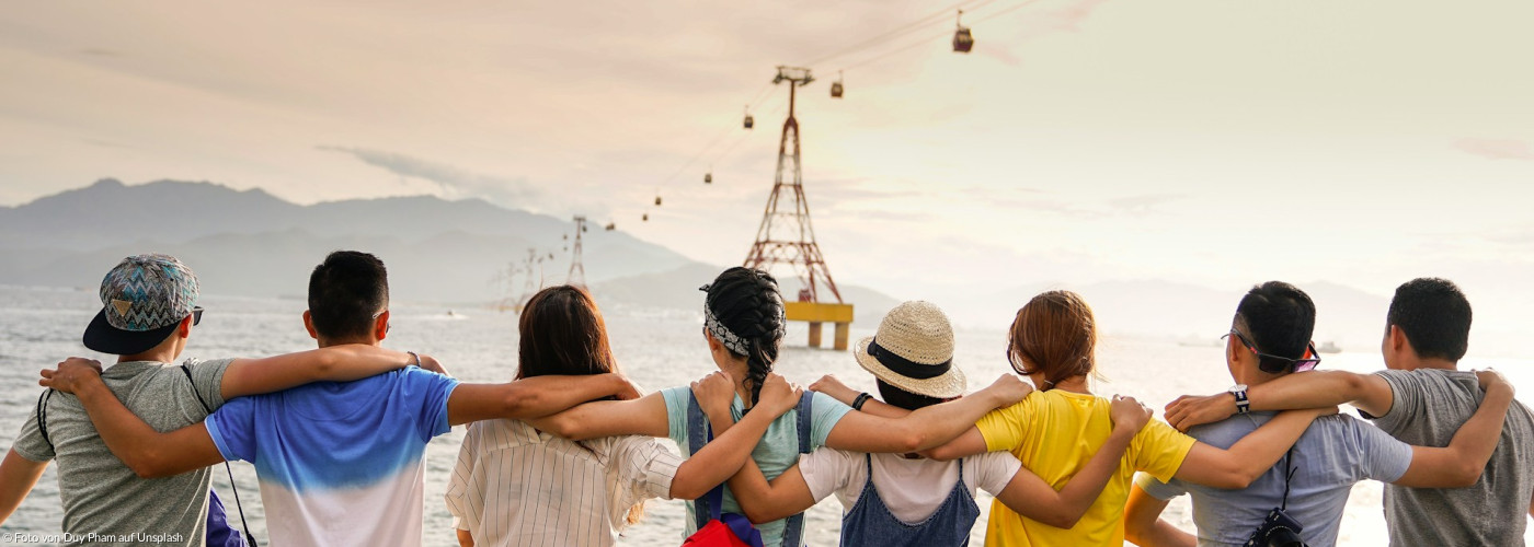8 Personen von hinten mit über der Schulter verschränkten Armen