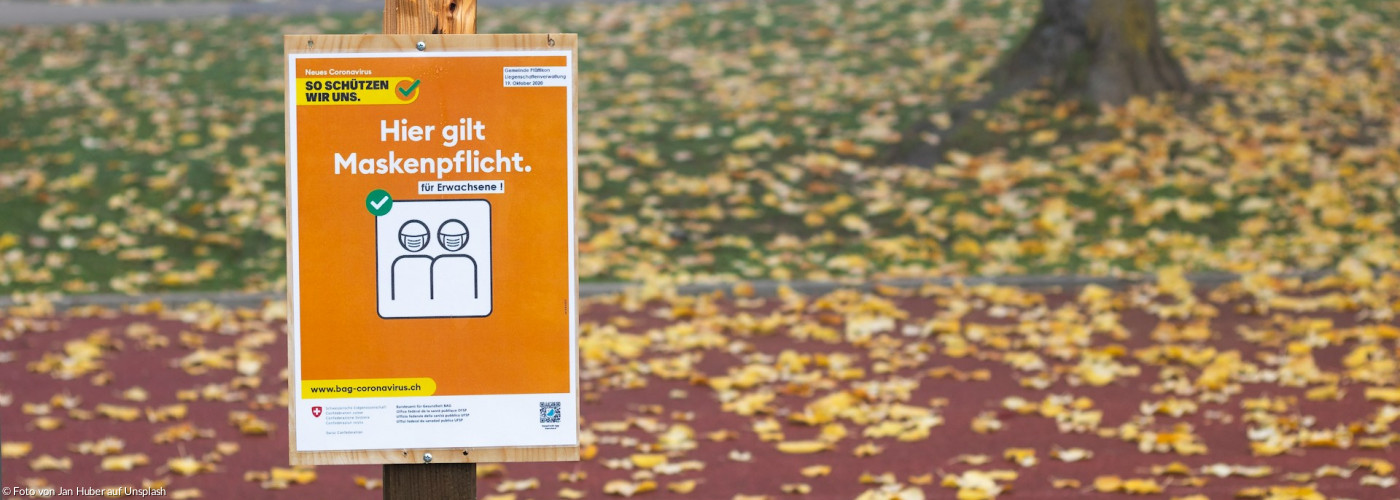 Braune Holzbeschilderung mit Aufschrift: "Hier gilt Maskenpflicht"