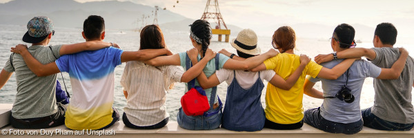 8 Menschen in einer Reihe, die sich die Arme gegenseitig auf die Schultern legen